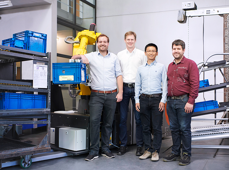 Ein Teil des Projektteams QBIIK (v.l.n.r.): Jonathan Dziedzitz (KIT IFL), Gerrit Flüssmeyer (Audi Sport), Yongzhou Zhang (KIT IAR) und Alexander Pollmann (Bär Automation) arbeiten gemeinsam an der autonomen Logistik.